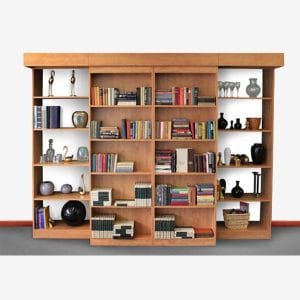Full-wall library shelving unit that hides a secret double murphy bed behind sliding bookshelves